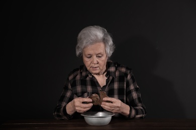 Photo of Poor mature woman with bread and bowl at table