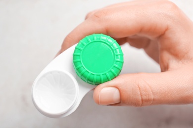 Photo of Woman holding contact lens case on light background, closeup