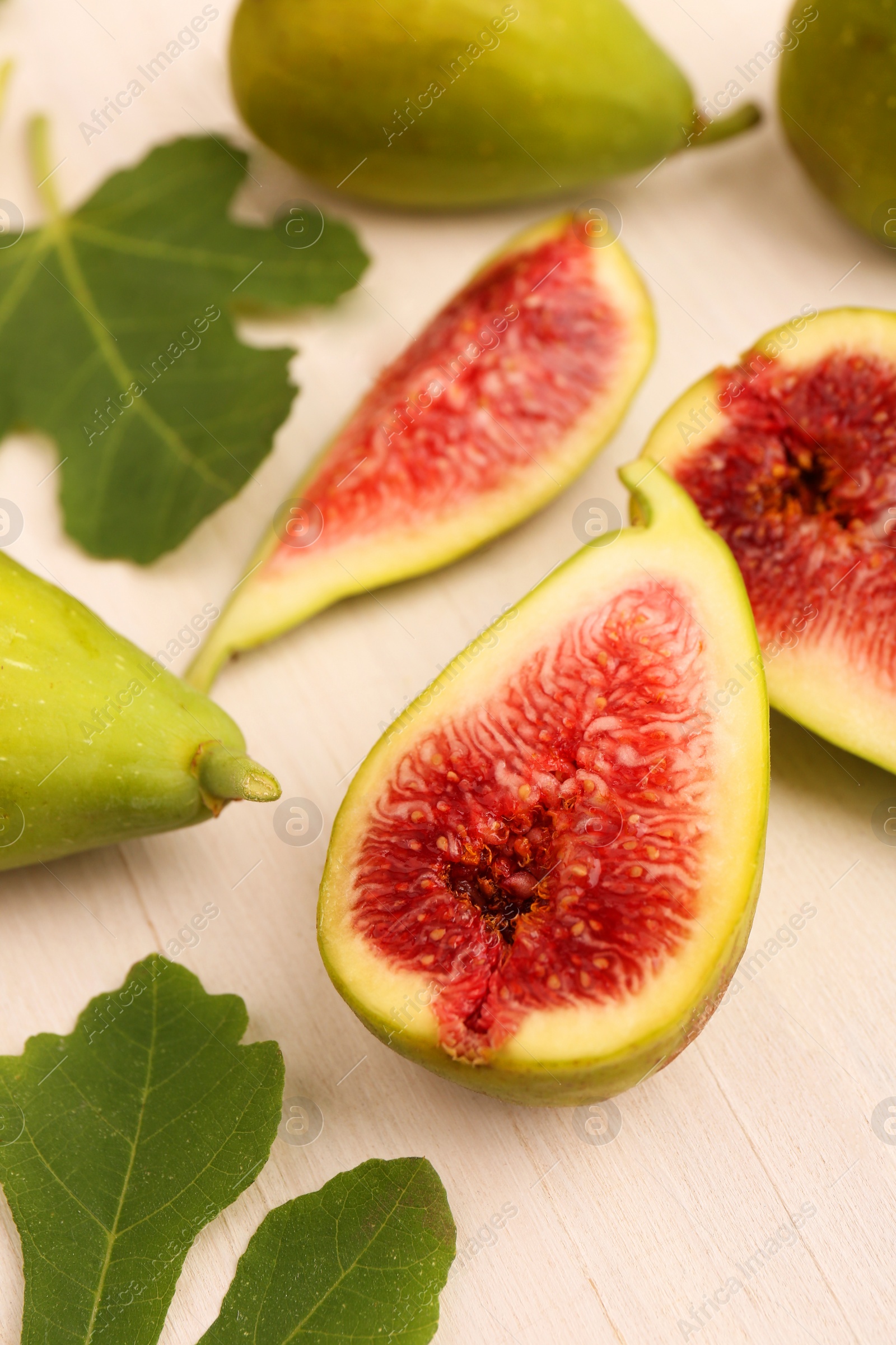 Photo of Cut and whole green figs with leaves on white wooden table, closeup