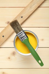 Photo of Can of yellow paint with brush on wooden table, top view