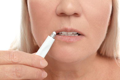 Image of Woman with cold sore applying cream on lips against white background, closeup