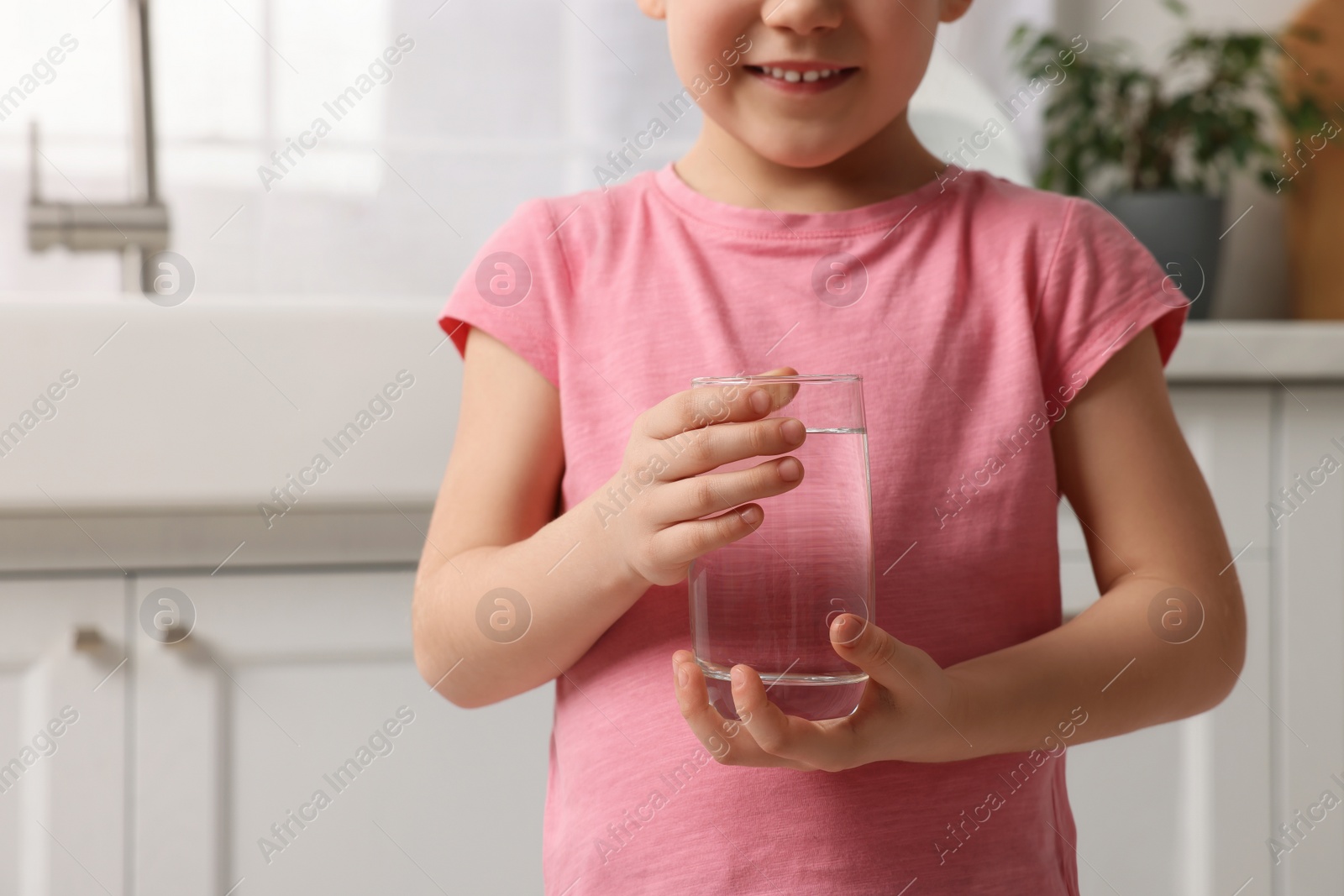 Photo of Little girl holding glass of fresh water at home, closeup. Space for text