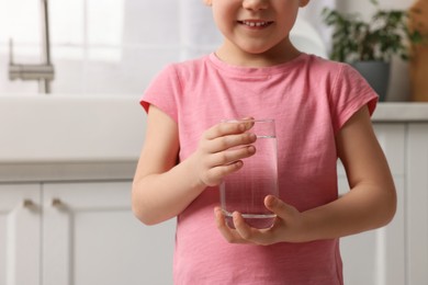 Little girl holding glass of fresh water at home, closeup. Space for text