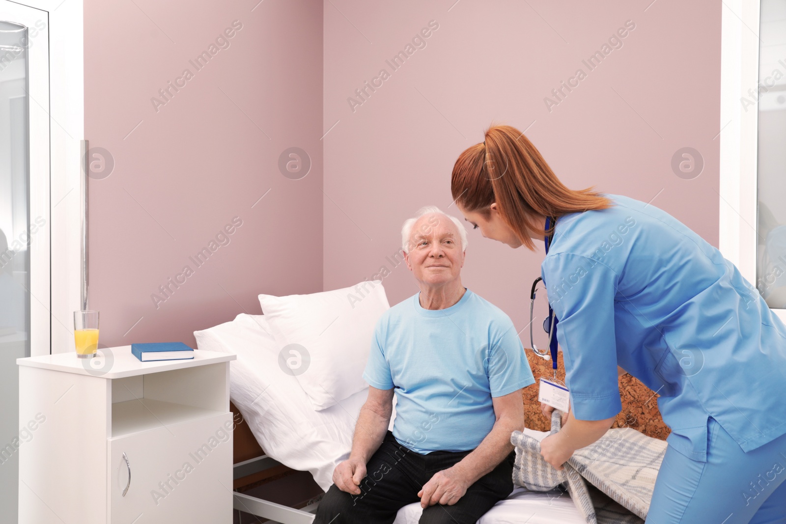 Photo of Nurse assisting senior man on bed in hospital ward