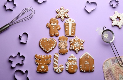 Photo of Christmas tree made of delicious gingerbread cookies surrounded by kitchen utensils on lilac background, flat lay