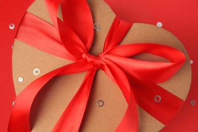 Photo of Beautiful heart shaped gift box with bow and confetti on red background, closeup