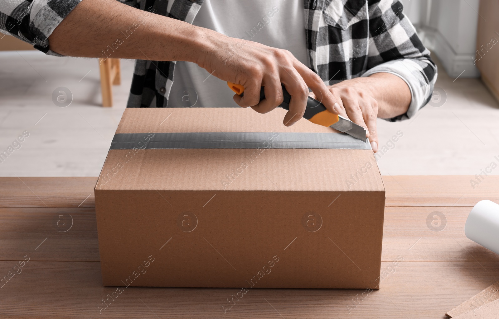 Photo of Man using utility knife to open parcel at wooden table, closeup