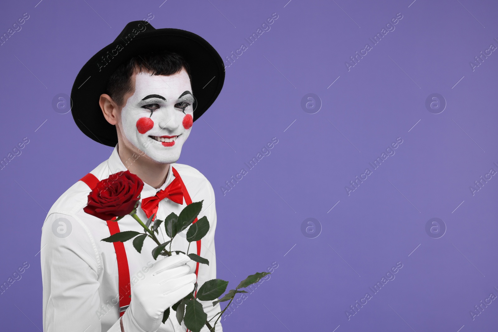 Photo of Funny mime artist with red rose on purple background. Space for text