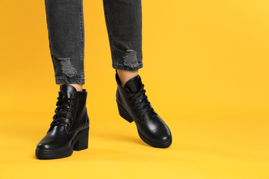 Photo of Woman wearing stylish boots on yellow background, closeup. Space for text