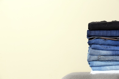 Photo of Stack of different jeans on ottoman against light background. Space for text