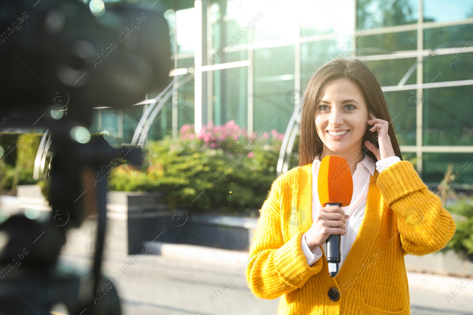 Photo of Young female journalist with microphone working on city street