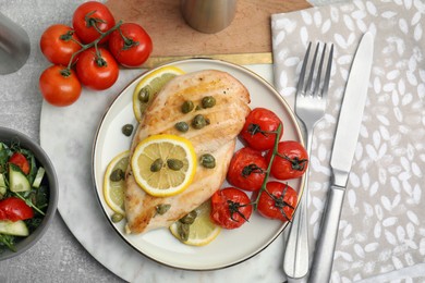 Delicious cooked chicken fillet with capers, tomatoes and lemon served on light grey table, flat lay