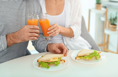 Young couple having breakfast with sandwiches at table in kitchen, closeup