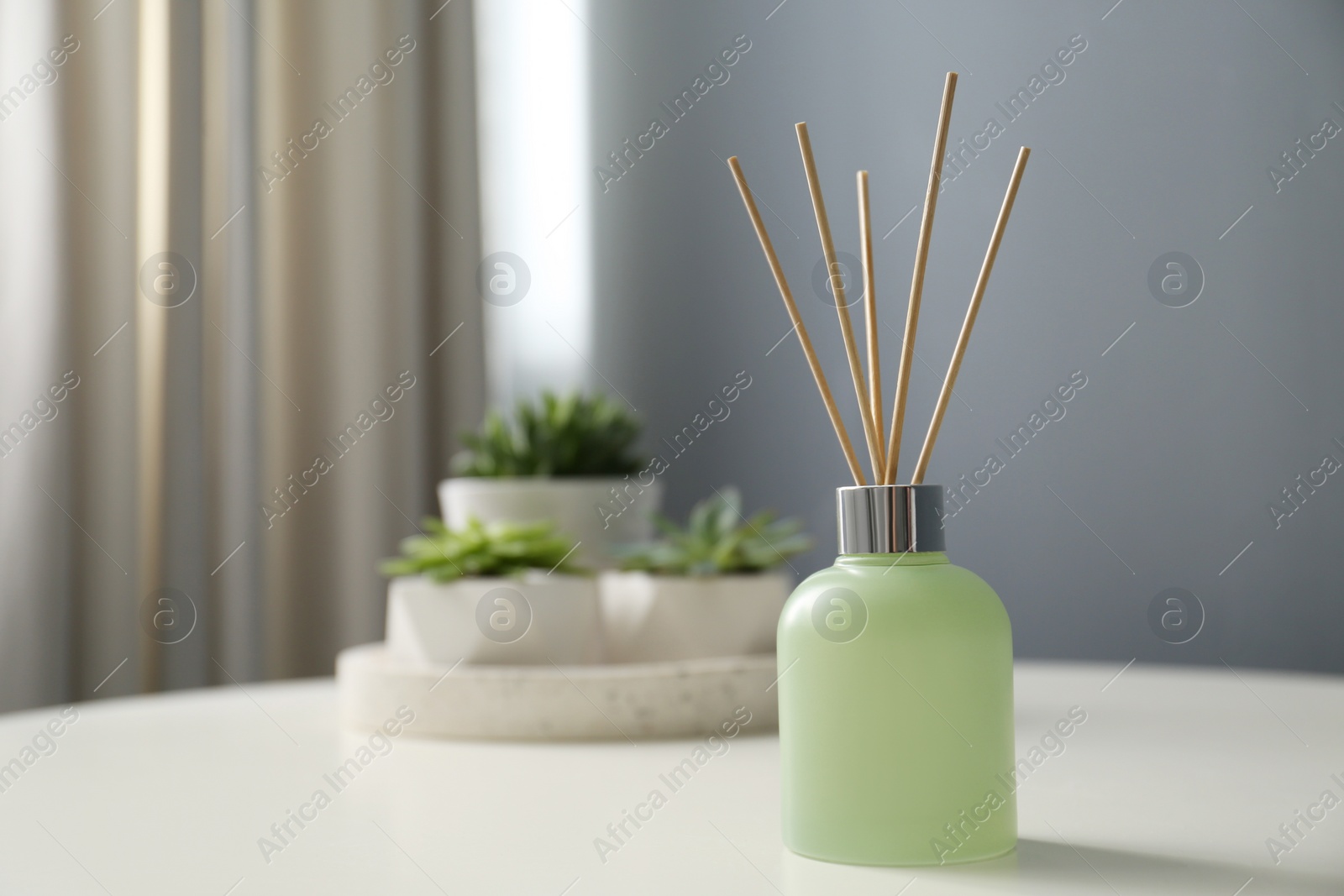 Photo of Aromatic reed air freshener on white table in room. Space for text