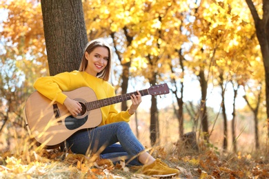 Teen girl playing guitar in autumn park
