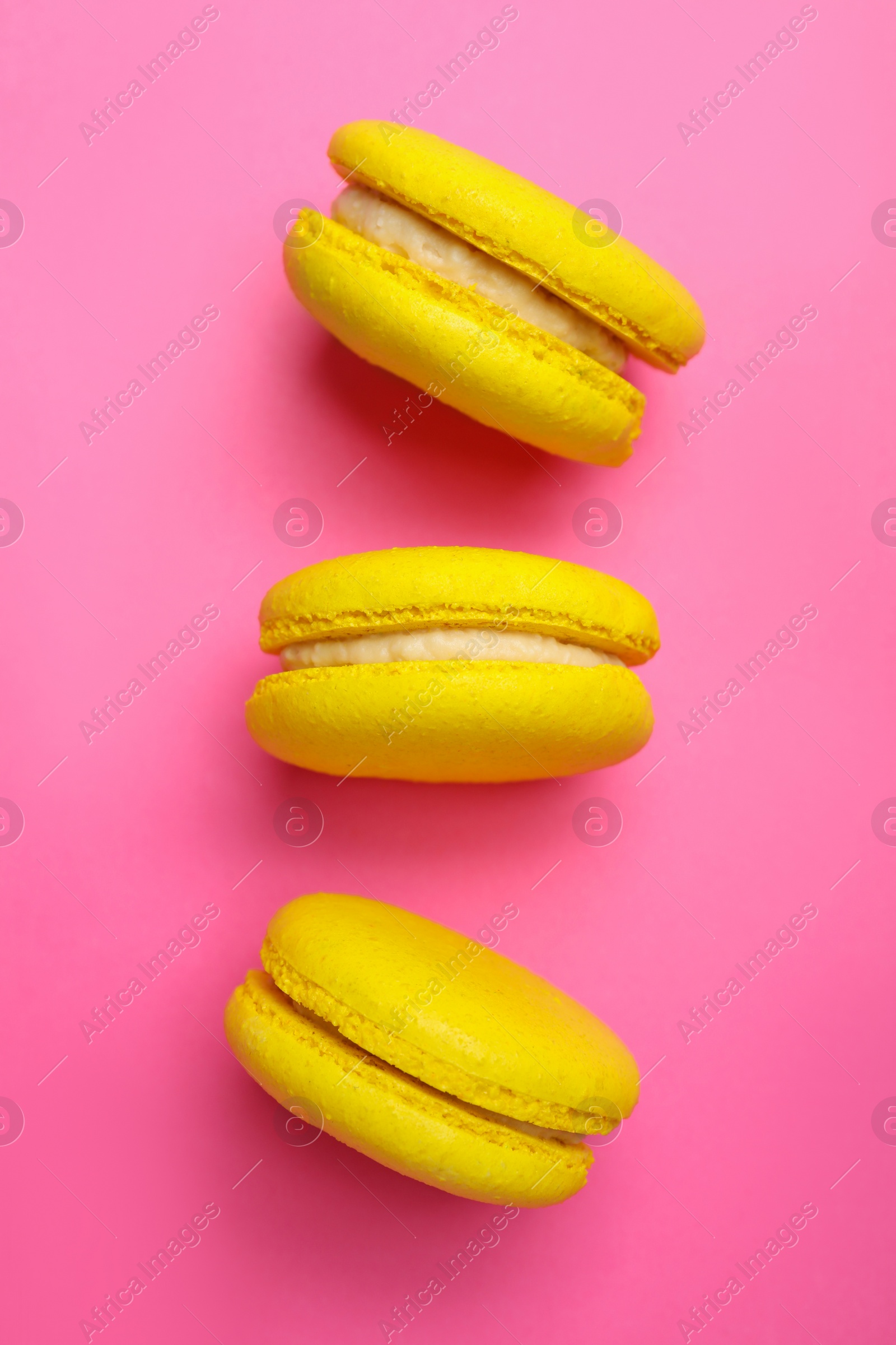 Photo of Delicious yellow macarons on pink background, flat lay