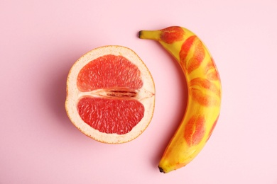 Fresh grapefruit and banana with red lipstick marks on pink background. Sex concept
