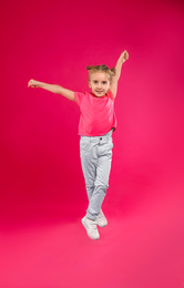 Photo of Cute little girl jumping on pink background
