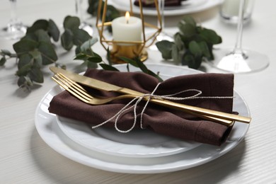 Photo of Stylish setting with cutlery and eucalyptus leaves on white wooden table, closeup