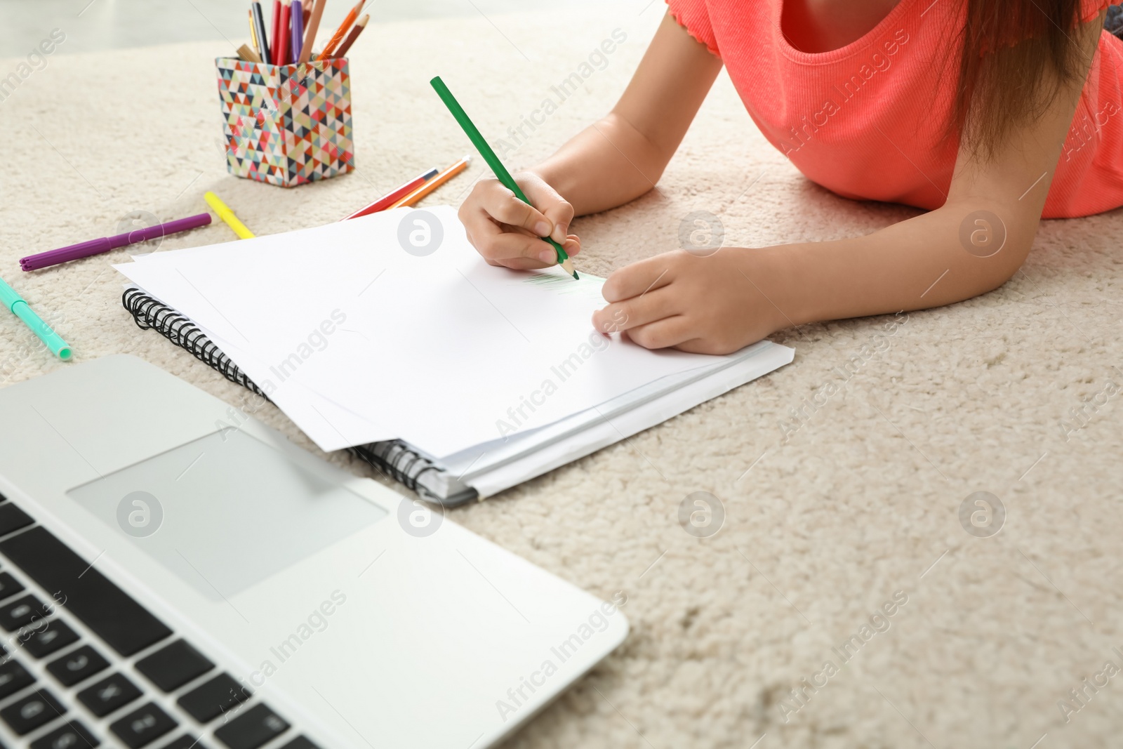 Photo of Little girl drawing on paper with pencil at online lesson indoors, closeup. Distance learning