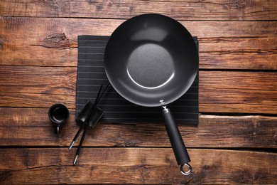 Empty iron wok, sauce bowl and chopsticks on wooden table, flat lay