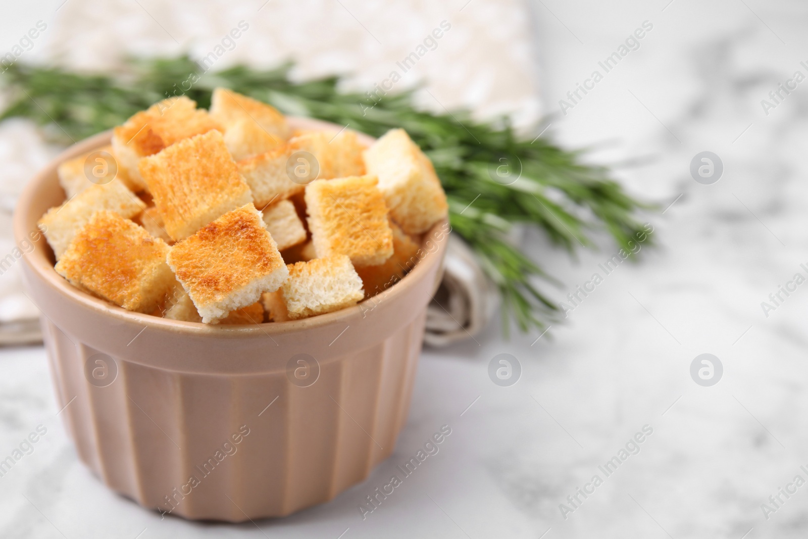 Photo of Delicious crispy croutons in bowl on white marble table, closeup