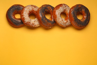 Photo of Many delicious fresh bagels on orange background, flat lay. Space for text