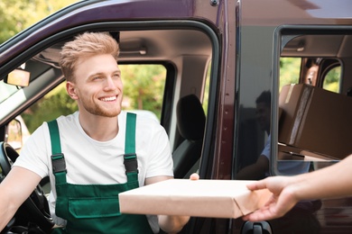 Photo of Young delivery courier giving parcel to customer outdoors