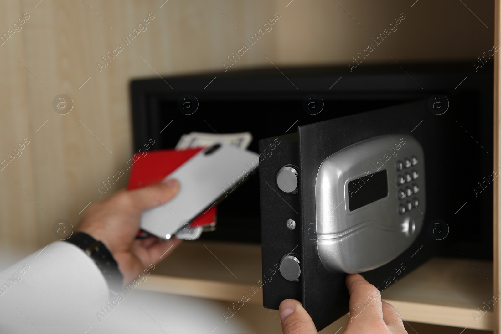 Photo of Man putting smartphone, passport and money into steel safe, closeup