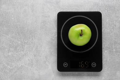 Digital kitchen scale with ripe green apple on grey table, top view. Space for text