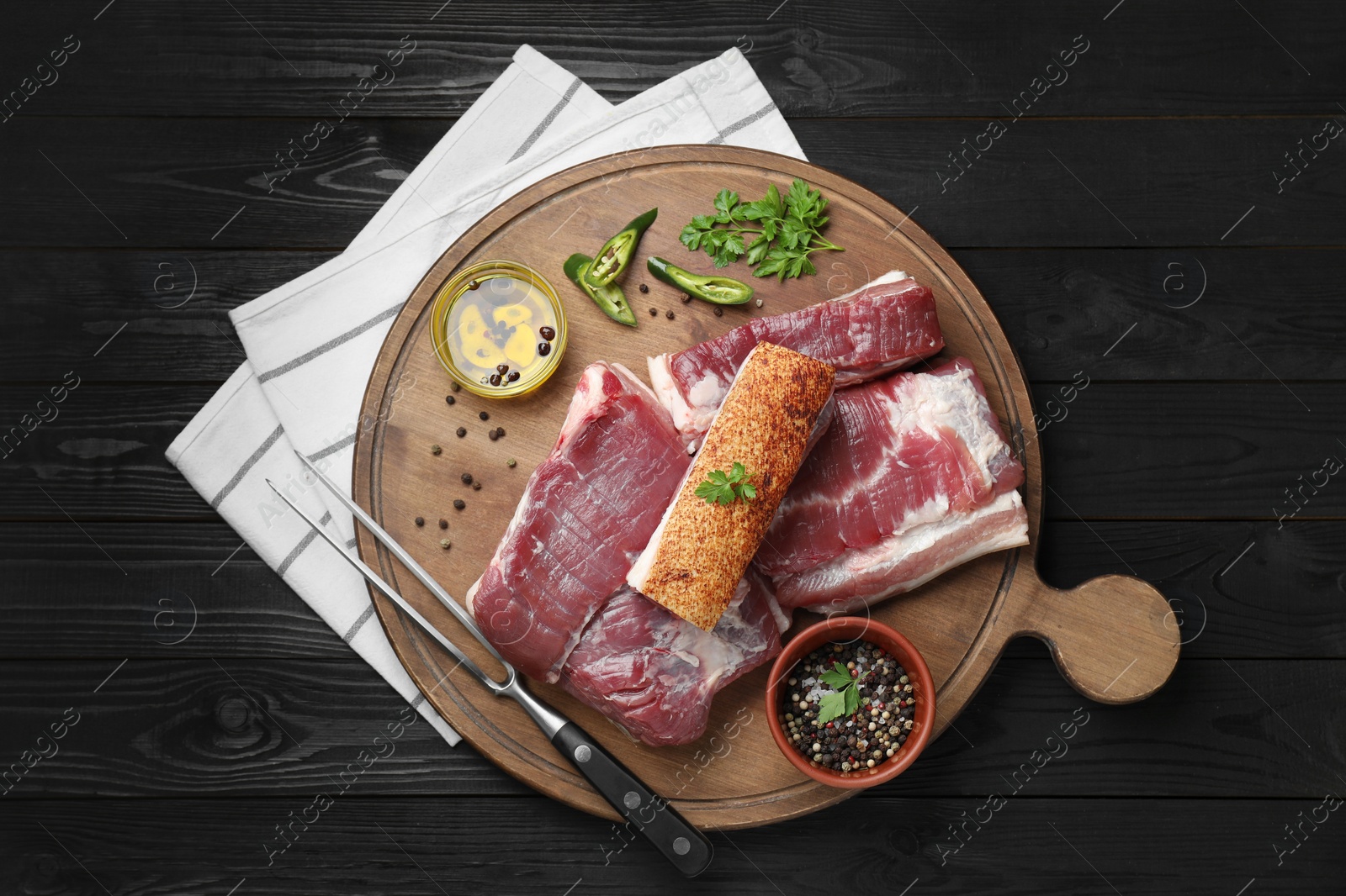 Photo of Pieces of raw pork belly, chili pepper, peppercorns, oil and parsley on black wooden table, top view