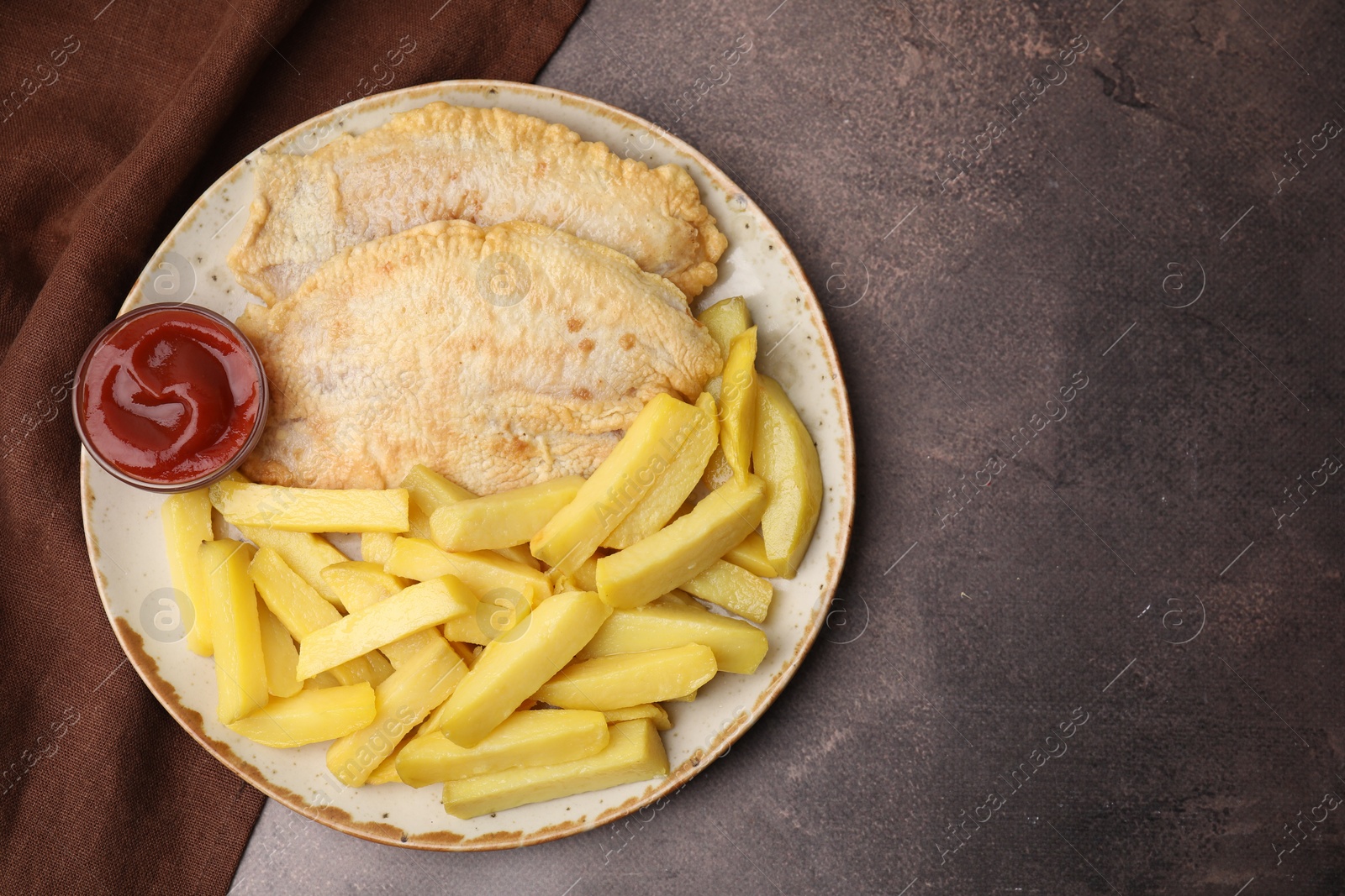 Photo of Delicious fish and chips with ketchup on brown table, top view. Space for text