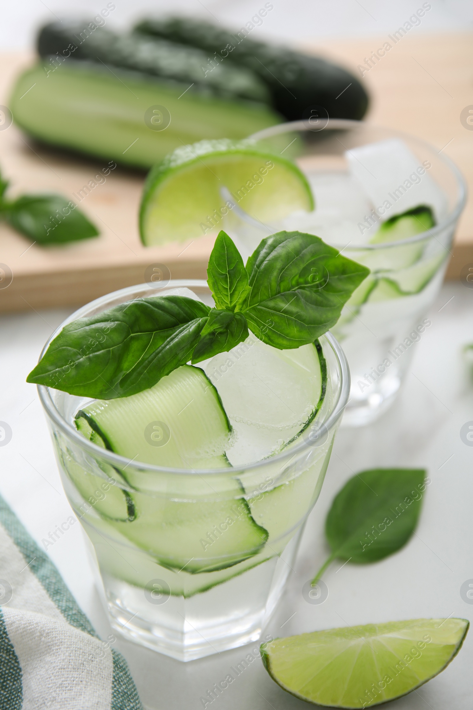 Photo of Tasty fresh cucumber water with sliced lime and basil on white table, closeup