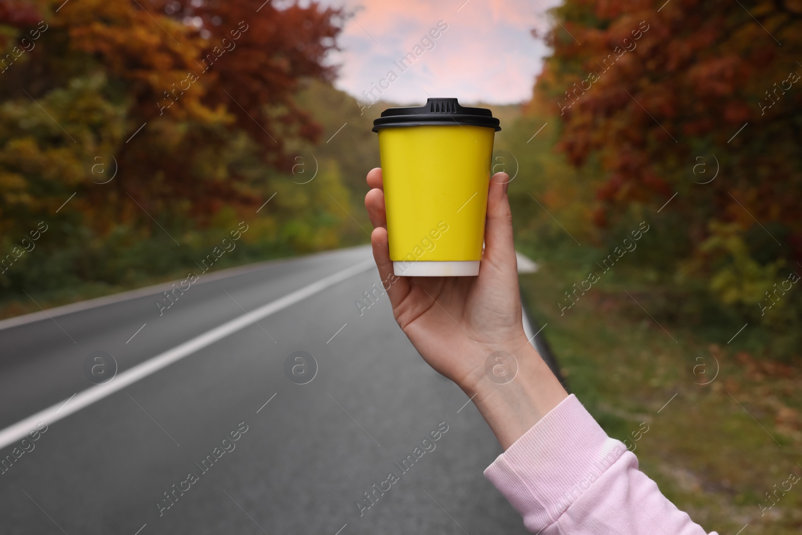 Photo of Woman holding takeaway cardboard coffee cup near road outdoors, closeup. Autumn season