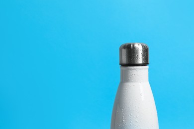 Photo of Stylish thermo bottle with water drops on blue background, closeup. Space for text