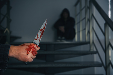 Photo of Man with bloody knife and scared person on stairs indoors, closeup. Dangerous criminal