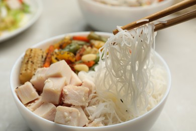 Chopsticks with tasty cooked rice noodles over bowl on table