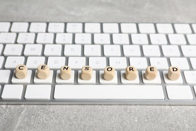 Photo of Wooden cubes with word Censored and keyboard on light grey table, closeup