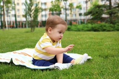 Photo of Adorable little baby sitting on blanket outdoors