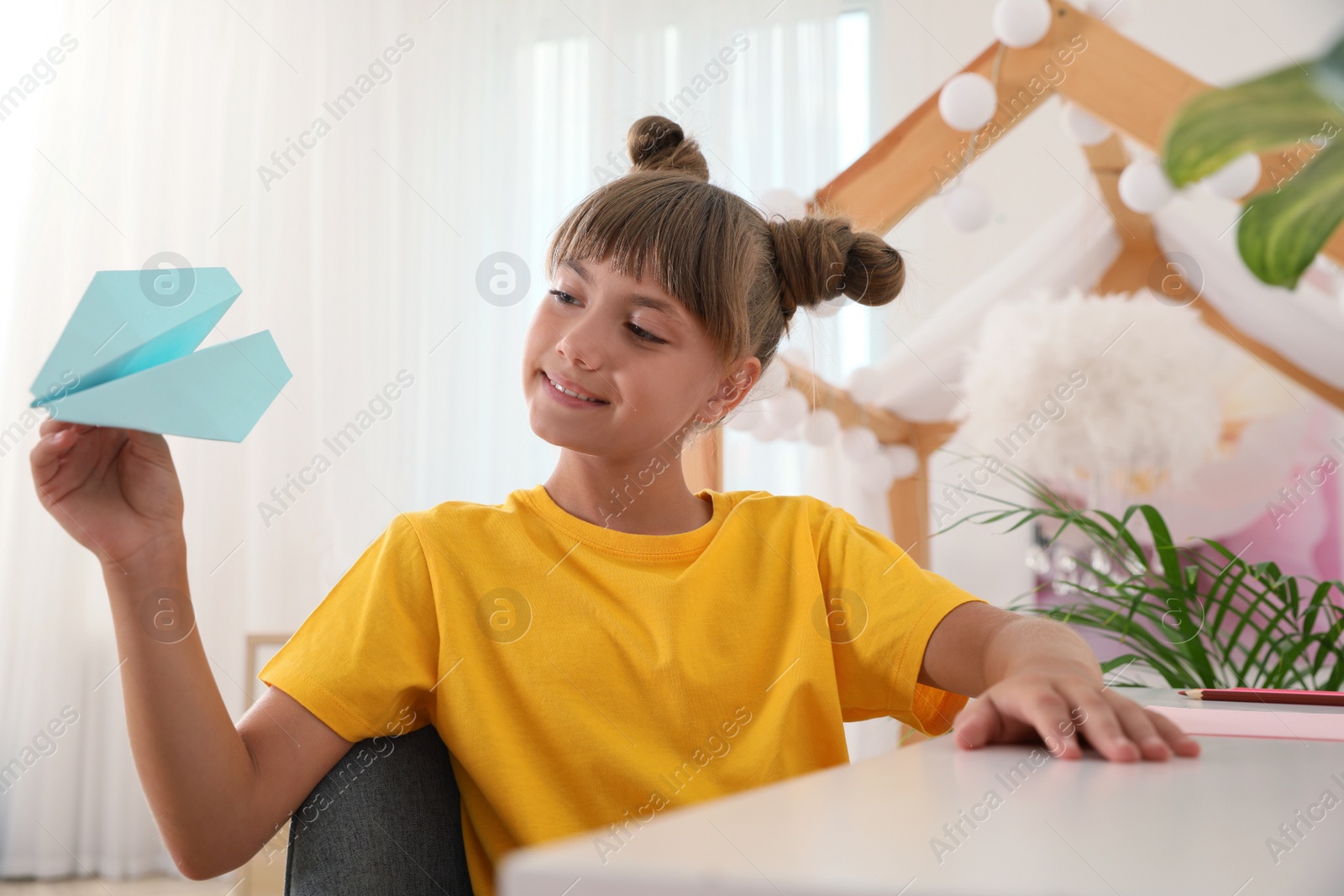 Photo of Cute little girl playing with paper plane at table in room