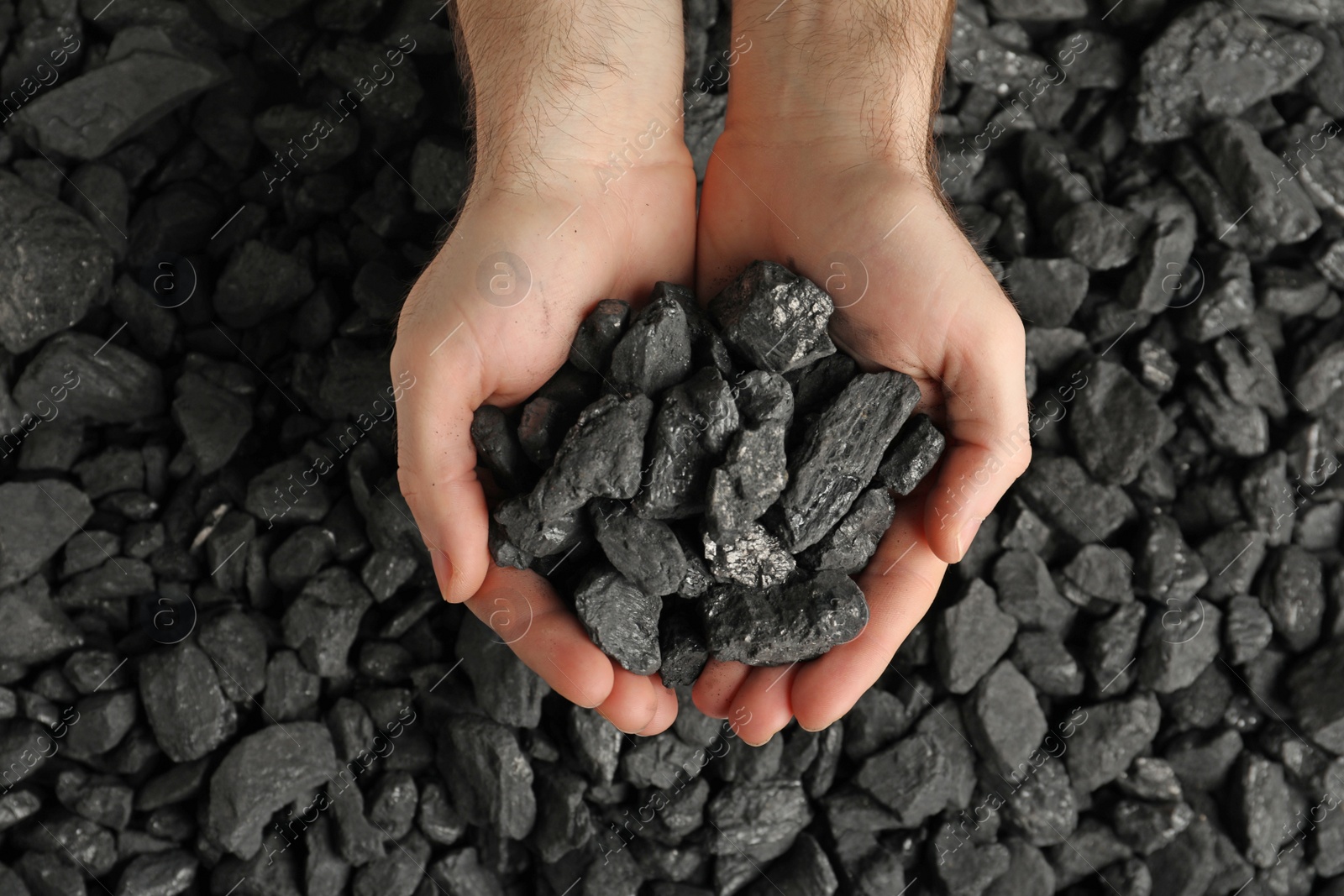 Photo of Man holding coal in hands over pile, top view