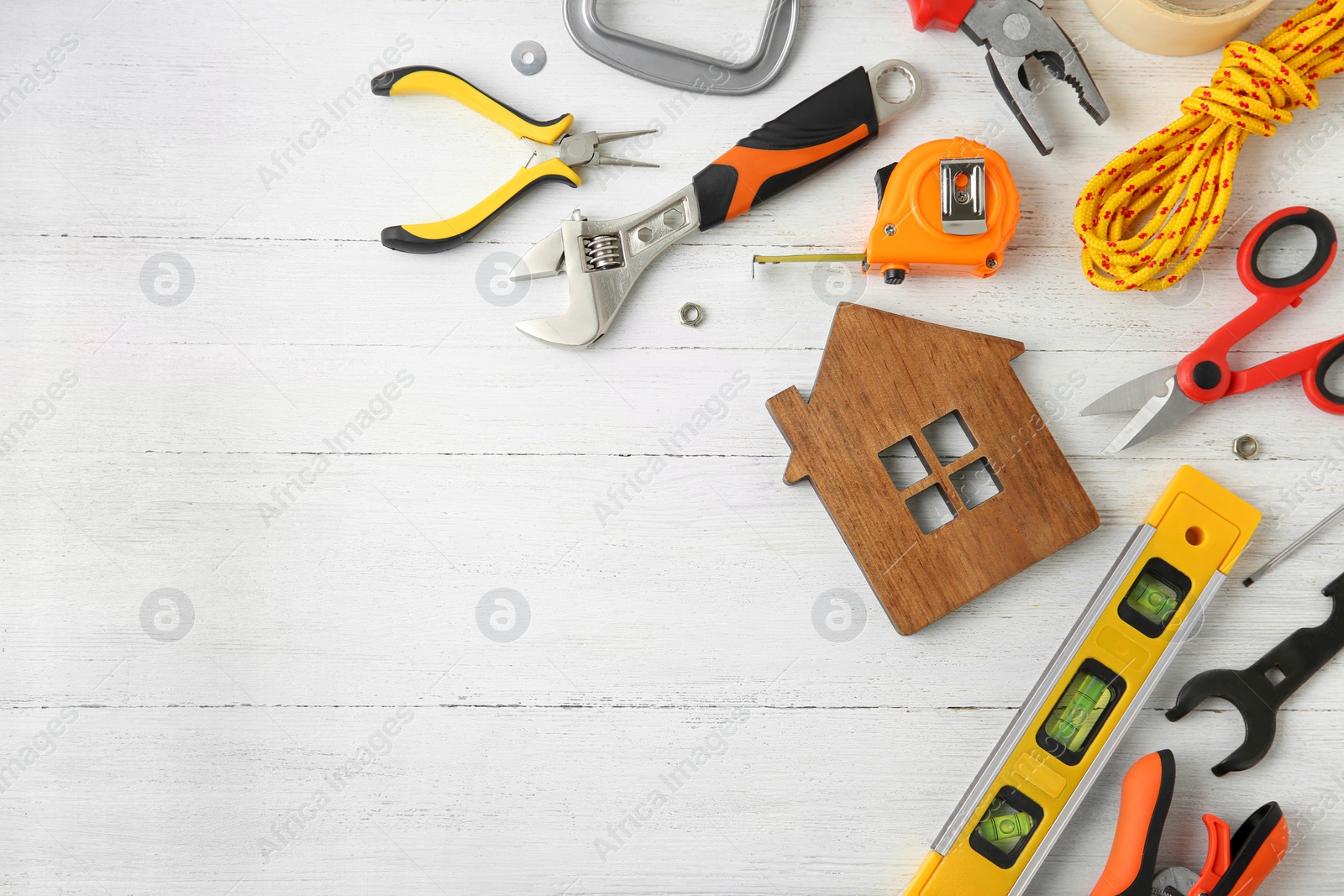 Photo of Set of repair tools and house figure on white wooden background, flat lay. Space for text