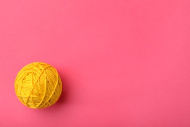 Photo of Soft yellow woolen yarn on pink background, top view. Space for text