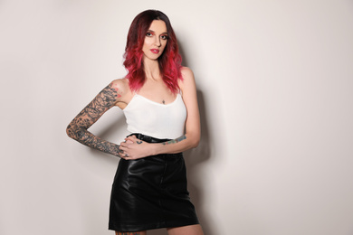 Beautiful woman with tattoos on arms against light background