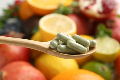 Photo of Vitamin pills in spoon against fresh fruits, closeup