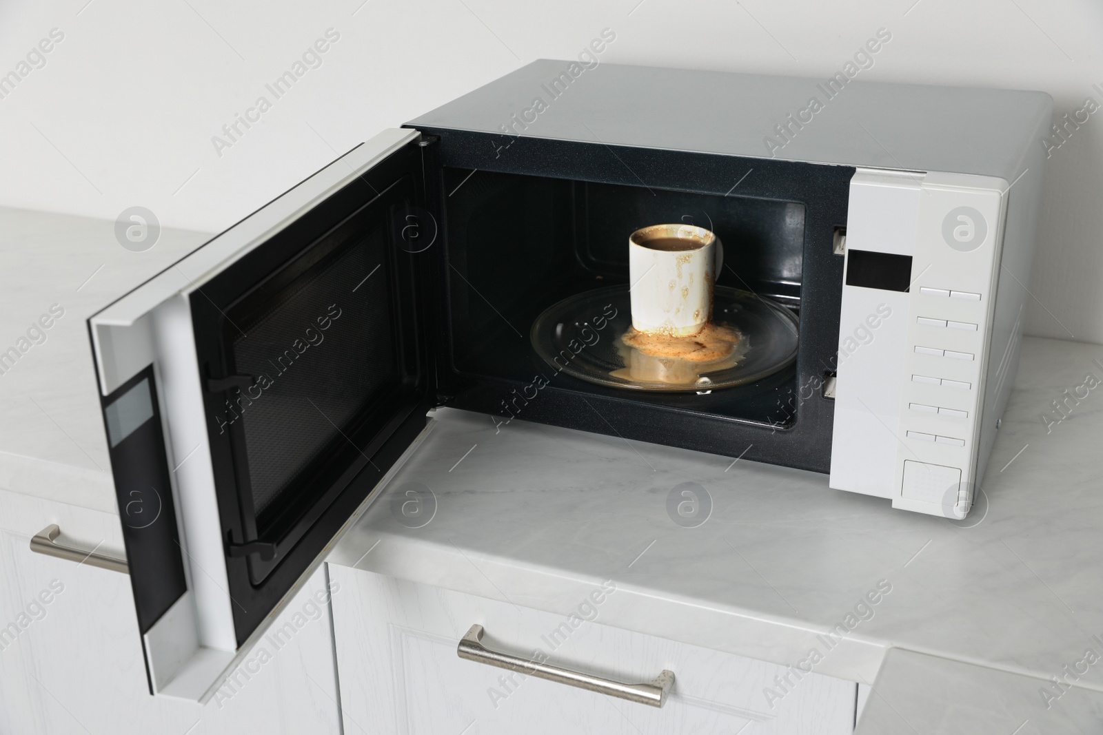 Photo of Dirty microwave oven with cup of coffee in kitchen