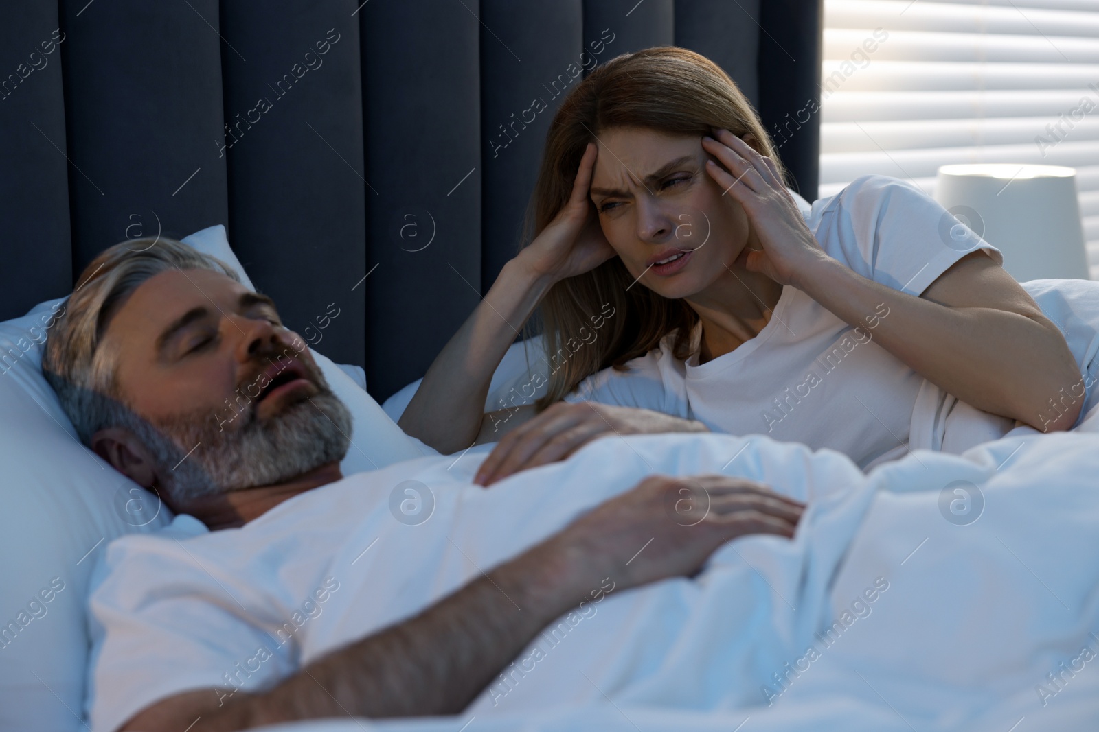 Photo of Irritated woman lying near her snoring husband in bed at home