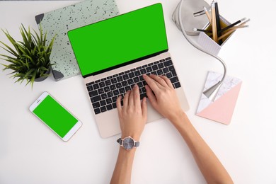 Image of Young woman using laptop at white desk, top view. Device display with chroma key