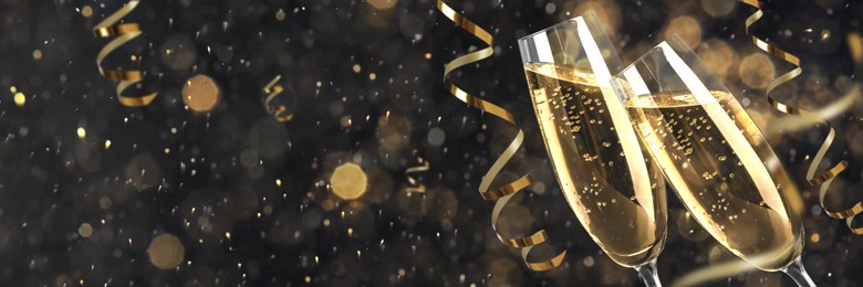 Image of Glasses with sparkling wine and shiny serpentine streamers against blurred festive lights, space for text. Banner design