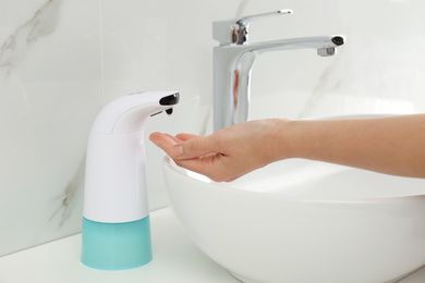 Woman using automatic soap dispenser in bathroom, closeup